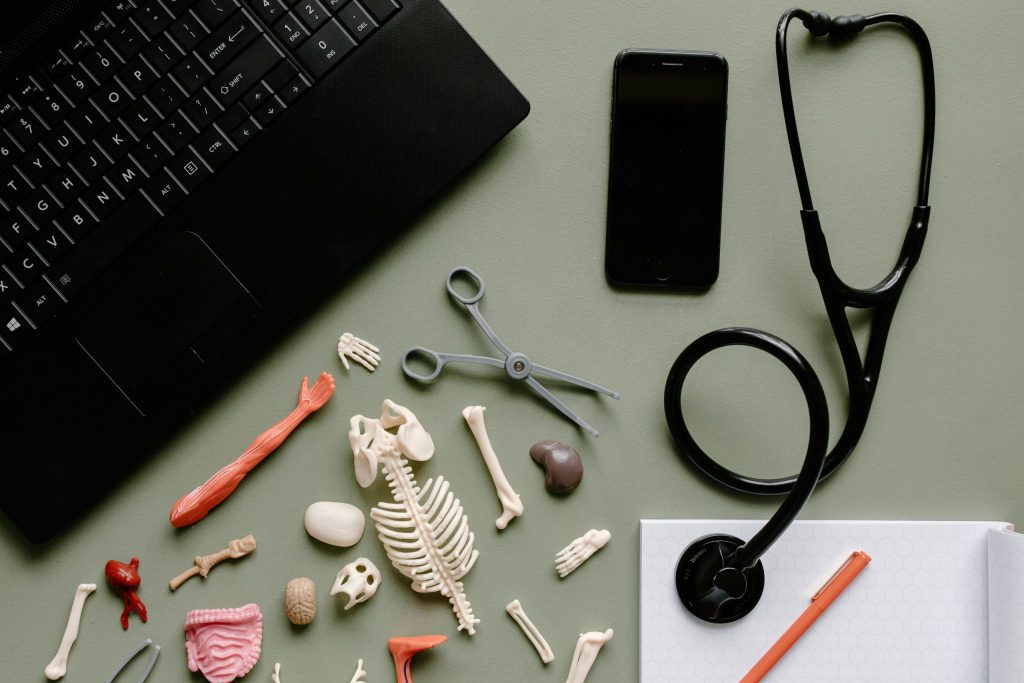 A desk with resources for an MCAT including anatomical models, a stethoscope, a smartphone, pencil and paper, and a laptop.