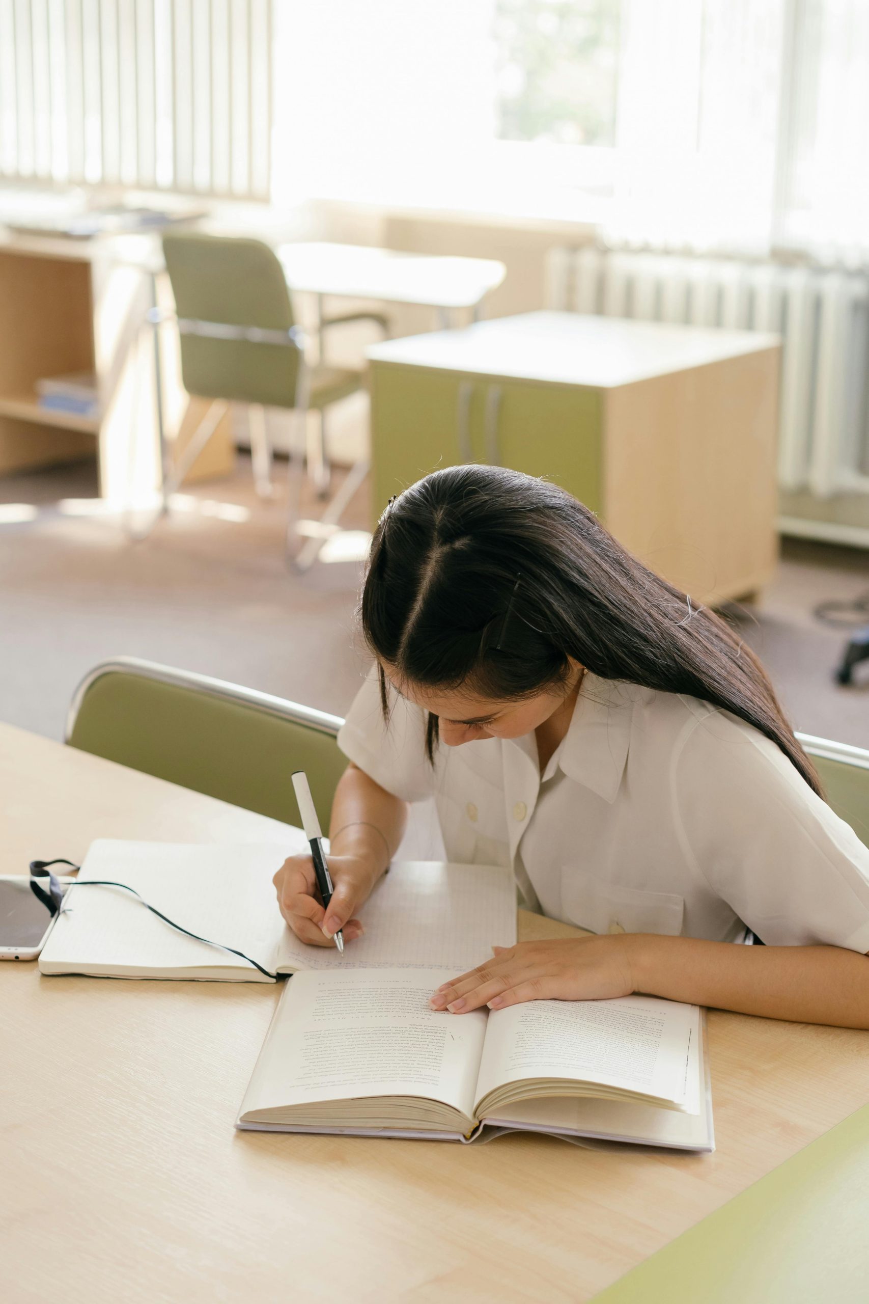 A woman writing her college admissions essays with a pencil on a notebook