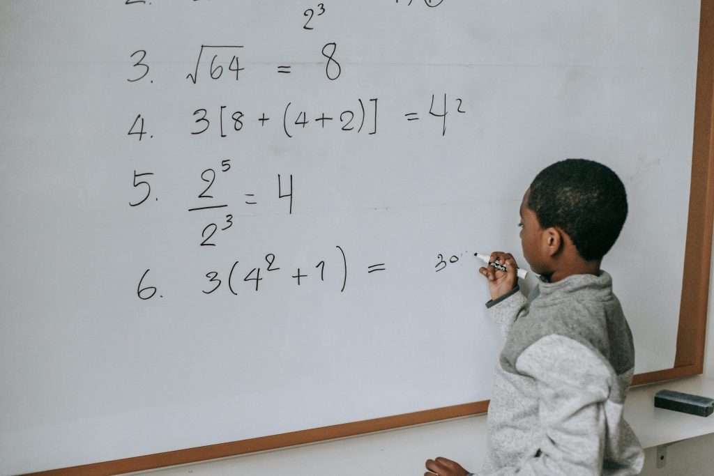 Elementary School student practicing math problems on a white board with a tutor.