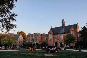 College students sitting on the grass while others tour the campus.