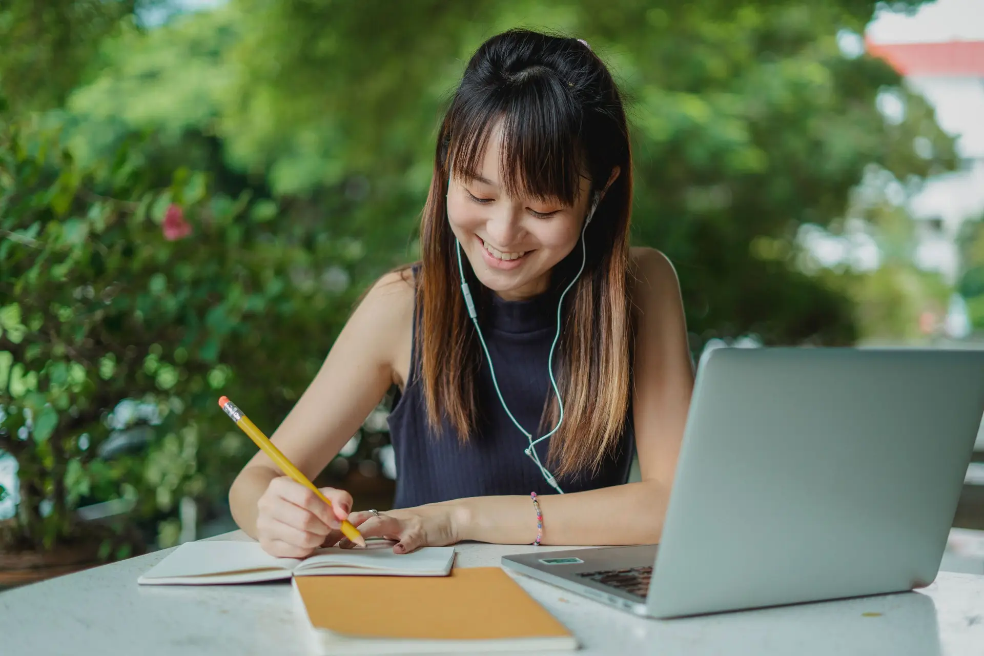 Student taking notes in a notebook while writing a supplemental college essay on their laptop.