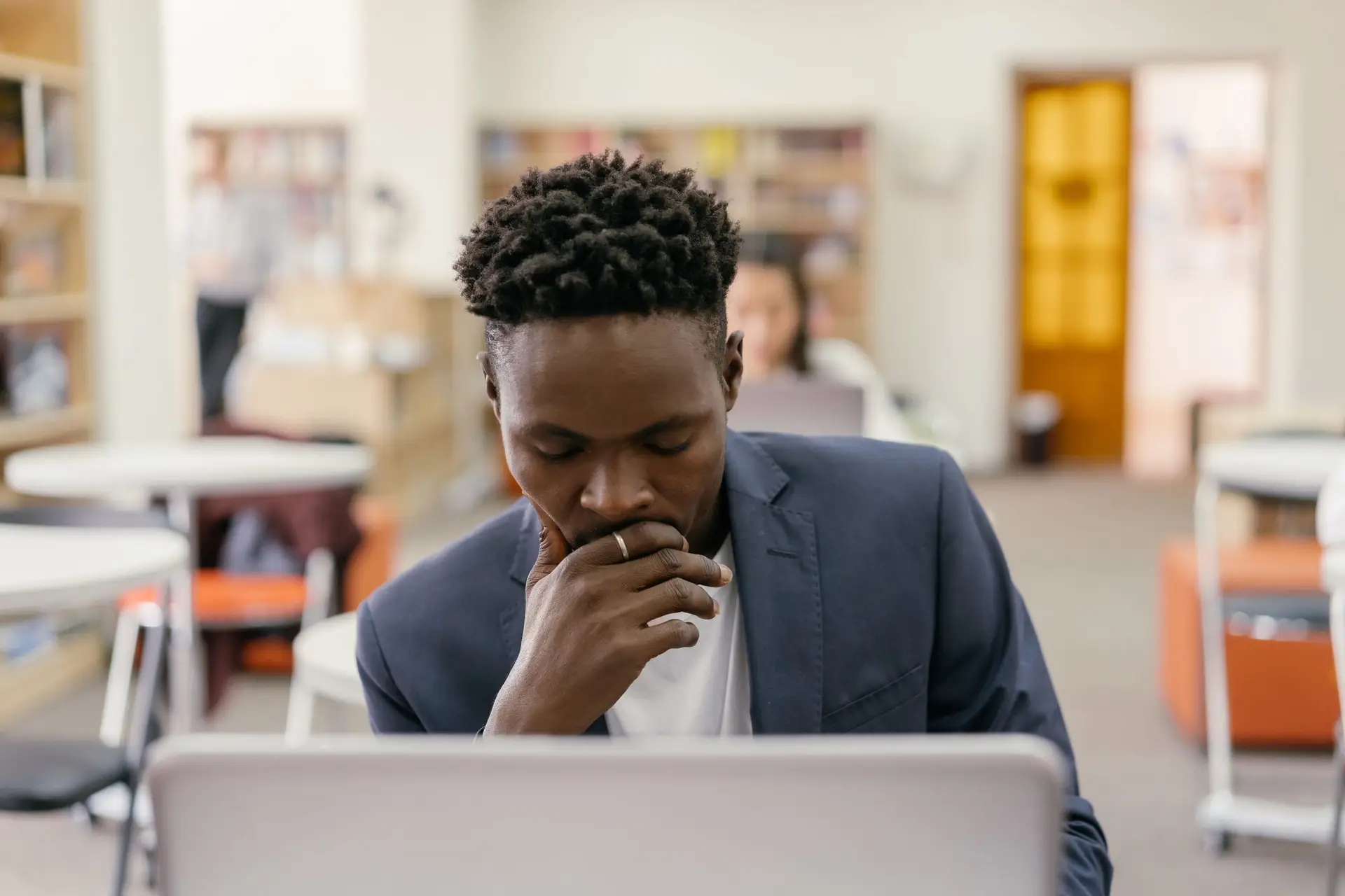 Male student looking at his computer in a classroom while he considers a college transfer.