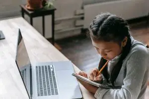 A middle school girl taking an ISEE from home on her computer while taking notes.